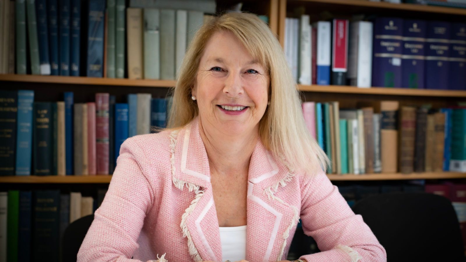 woman in pink suit top with long blond hair smiling at camera