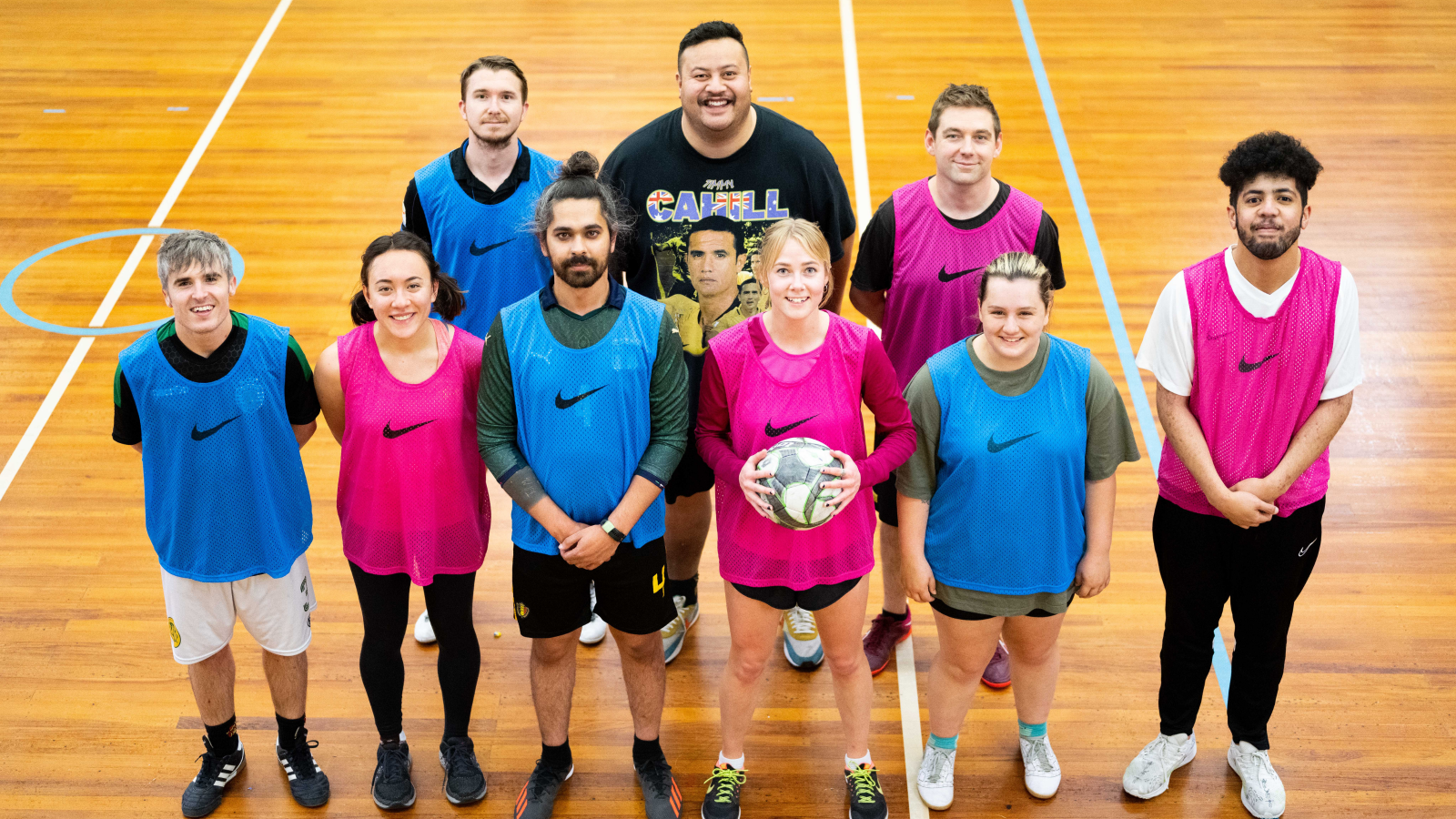 A group of people in sportswear stand on a court smiling at the camera.