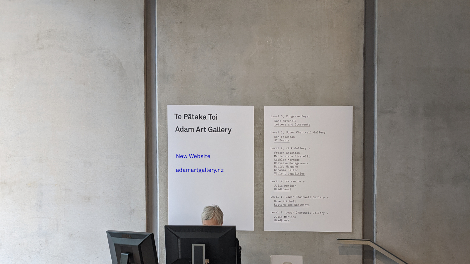 A woman at a desk with a poster behind her.