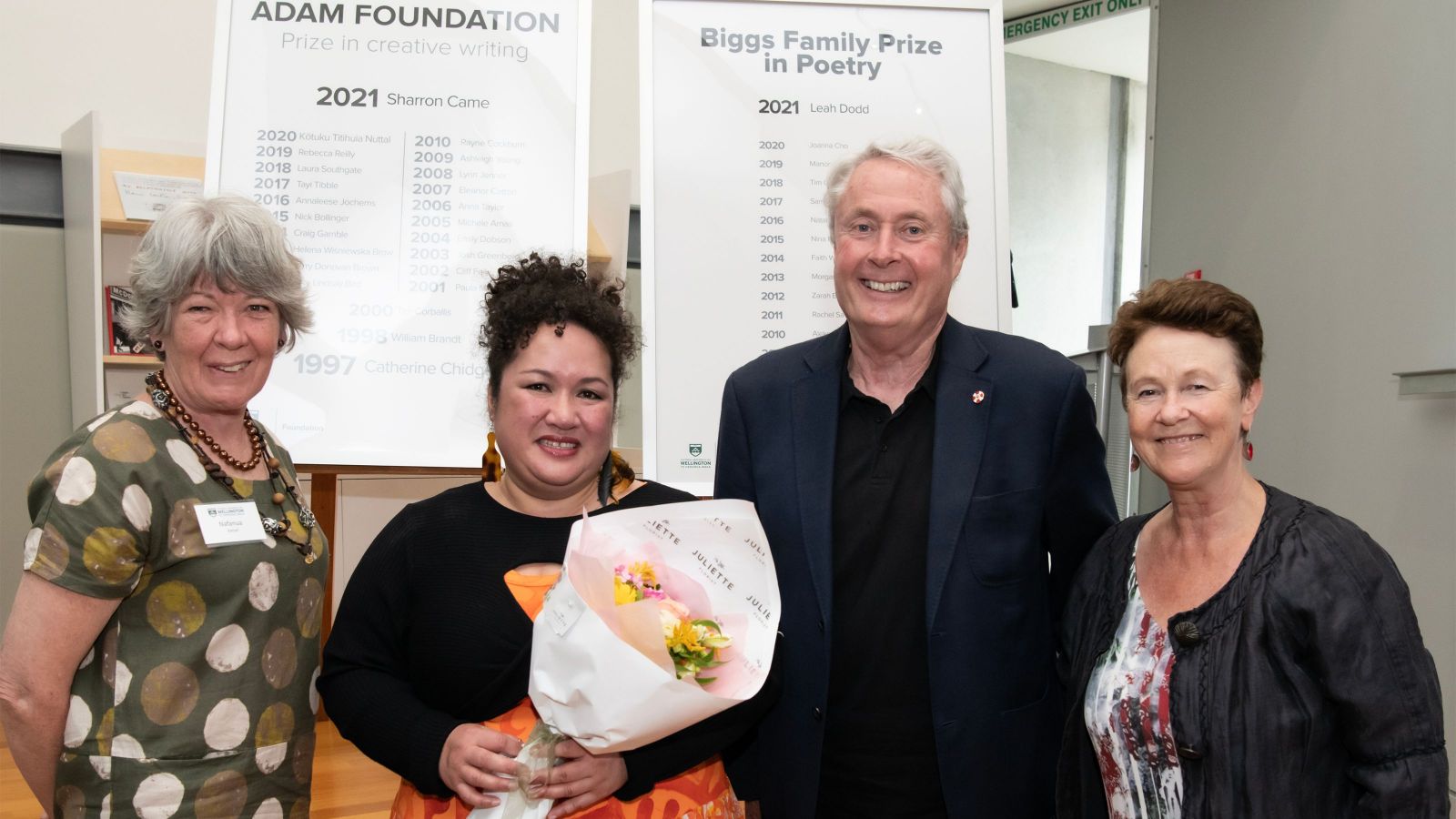 four people looking happy, one holding flowers