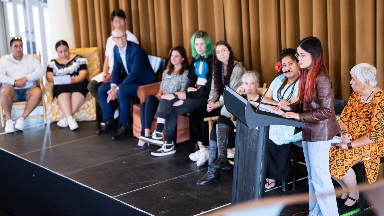 Student association member standing at a podium, with a group of people sat in a row behind her.