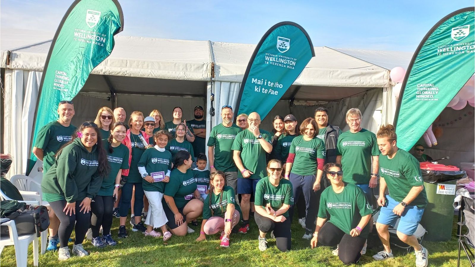 group of people with matching forest green t-shirts with 'te herenga waka victoria university of wellington' printed