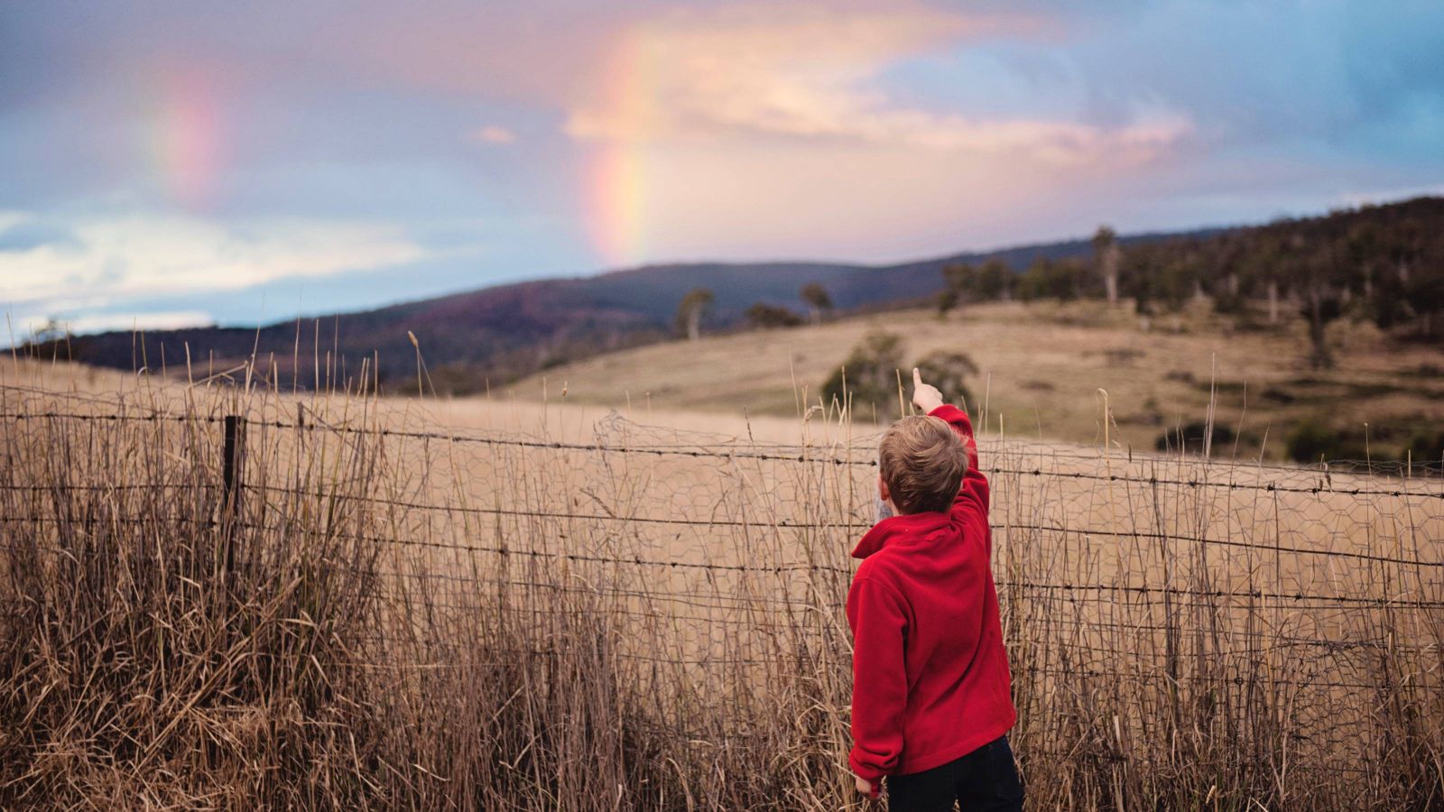 Child pointing at a rainbow in the sky 