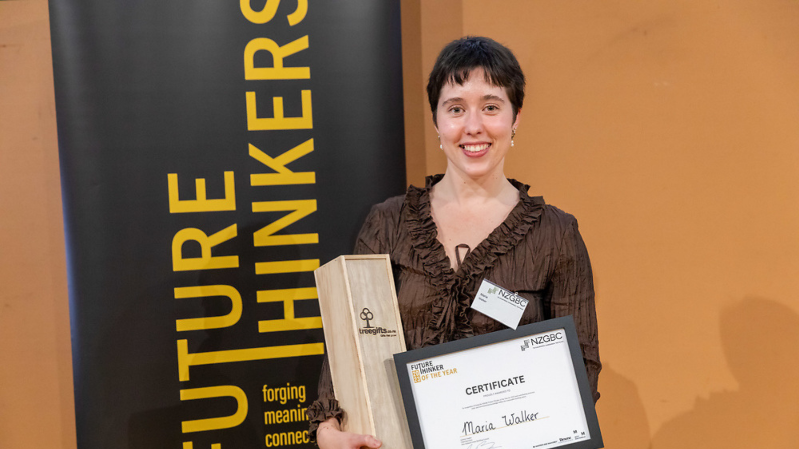 A young woman stands smiling at the camera holding a trophy and a certificate.