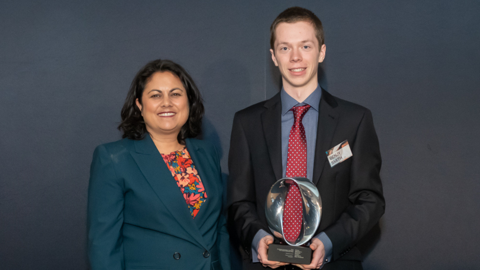 A young man stands holding a trophy with a government minister.