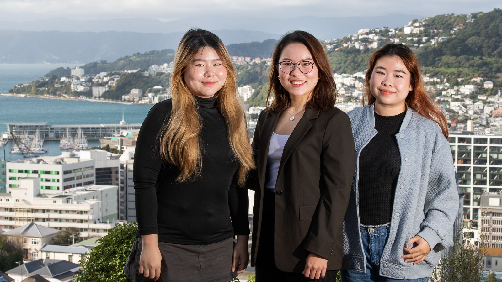 Three sisters from Vietnam, who study at Victoria University of Wellington in New Zealand, overlooking the iconic waterfront and city buildings.