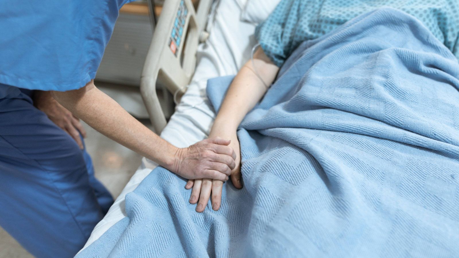 Person in blue scrubs holding the hand of a patient in hospital 