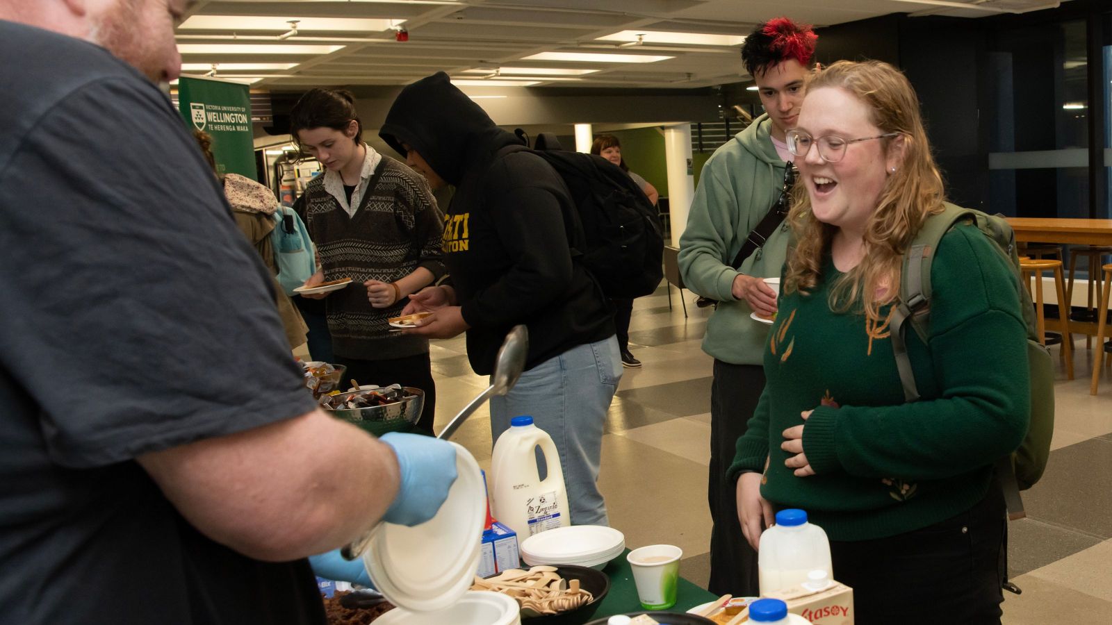 delighted looking blond student wearing forest green top receiving breakfast 