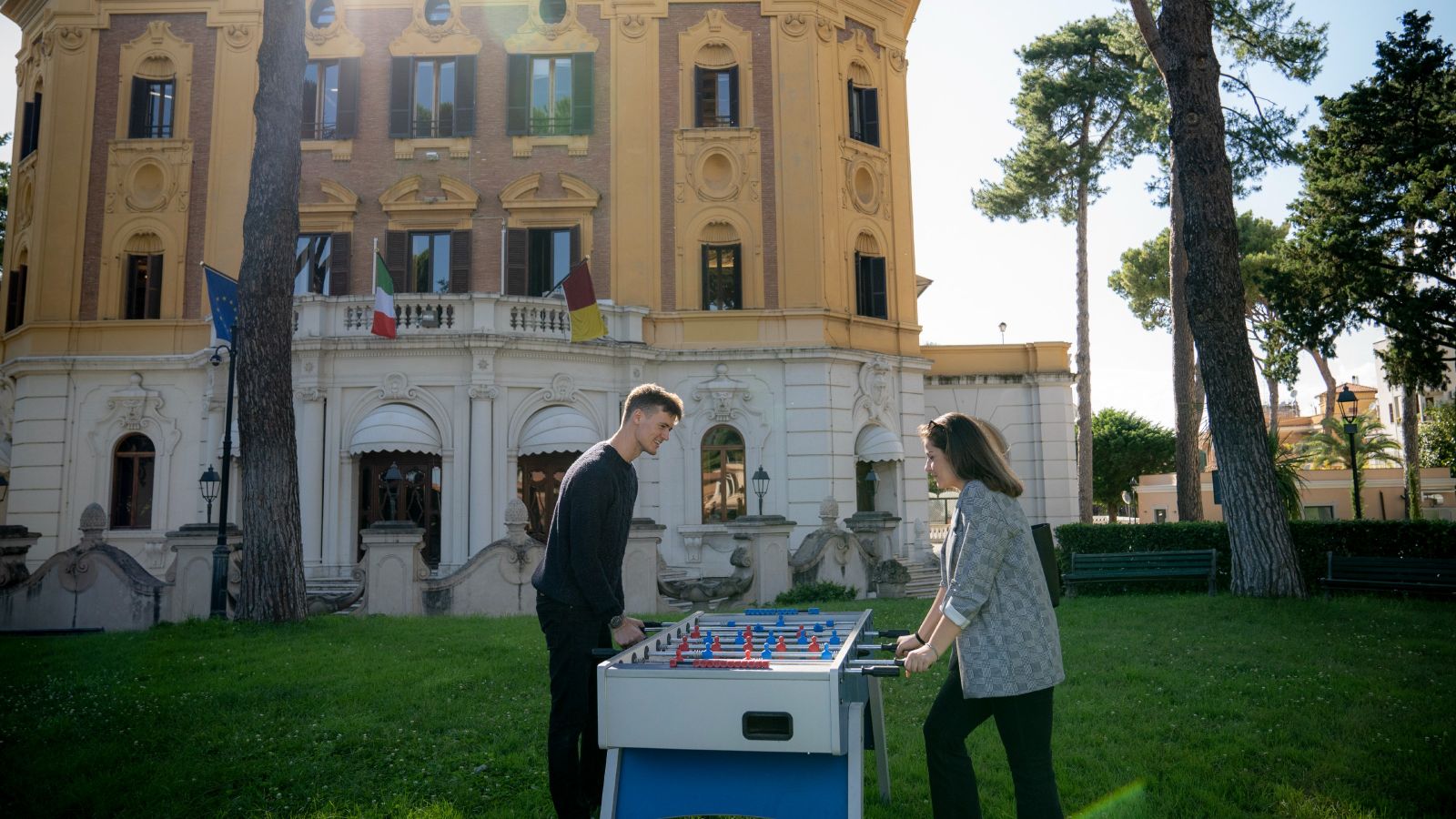 Two students are playing foosball on the lawn outside an old building at LUISS university in Rome.
