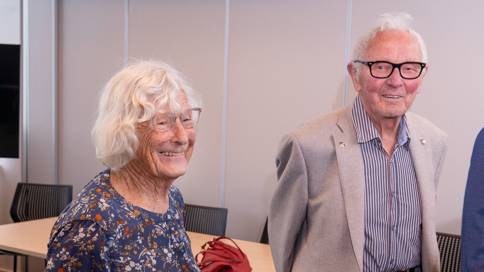 Sir Mark Dunajtschik and Dorothy Spotswood are standing indoors and smiling. 