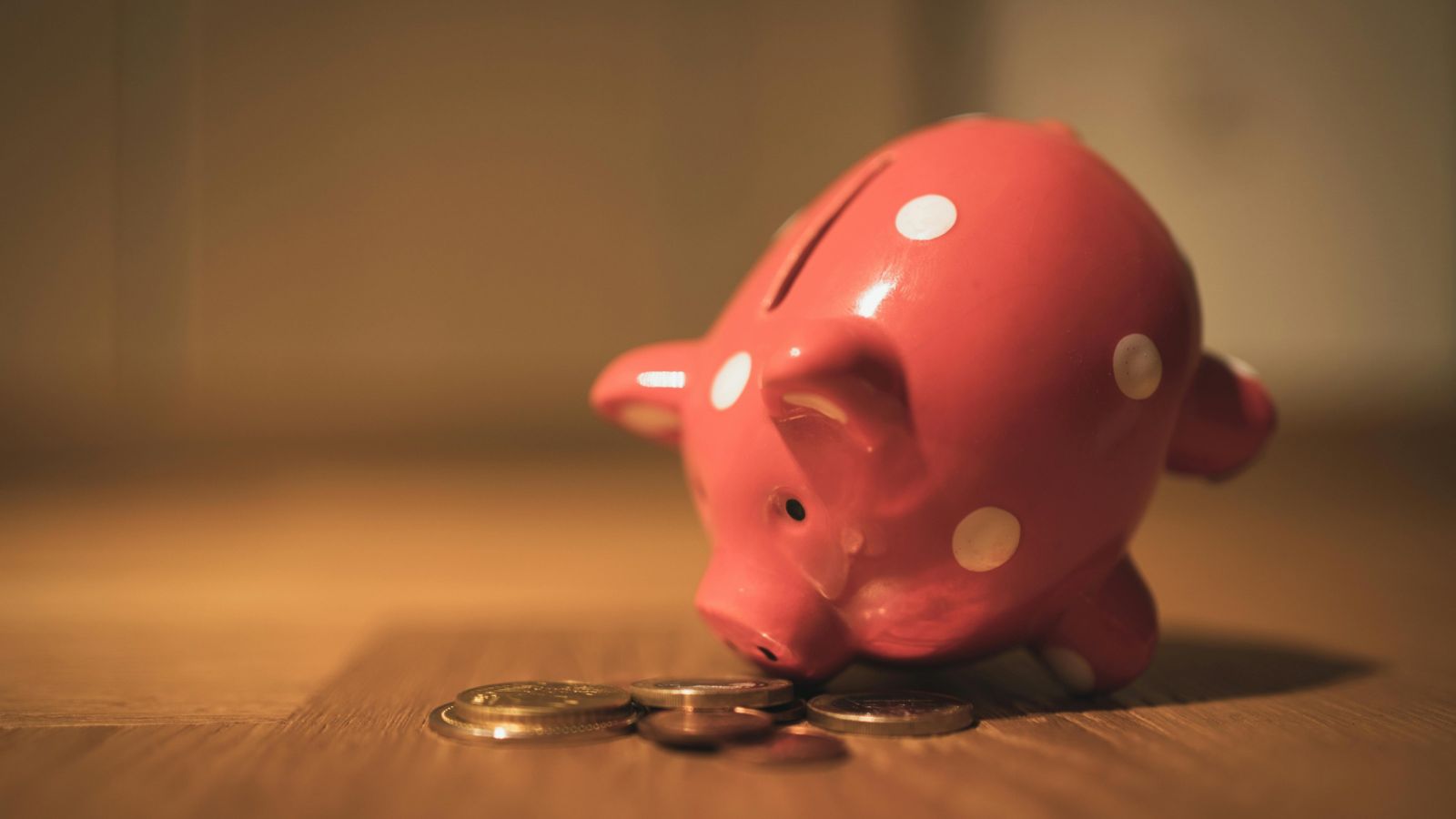 Pink piggy bank lying beside coins 