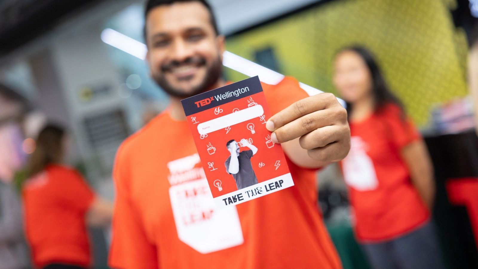 A TEDx volunteer holds out a branded lanyard towards the camera, showing the logo