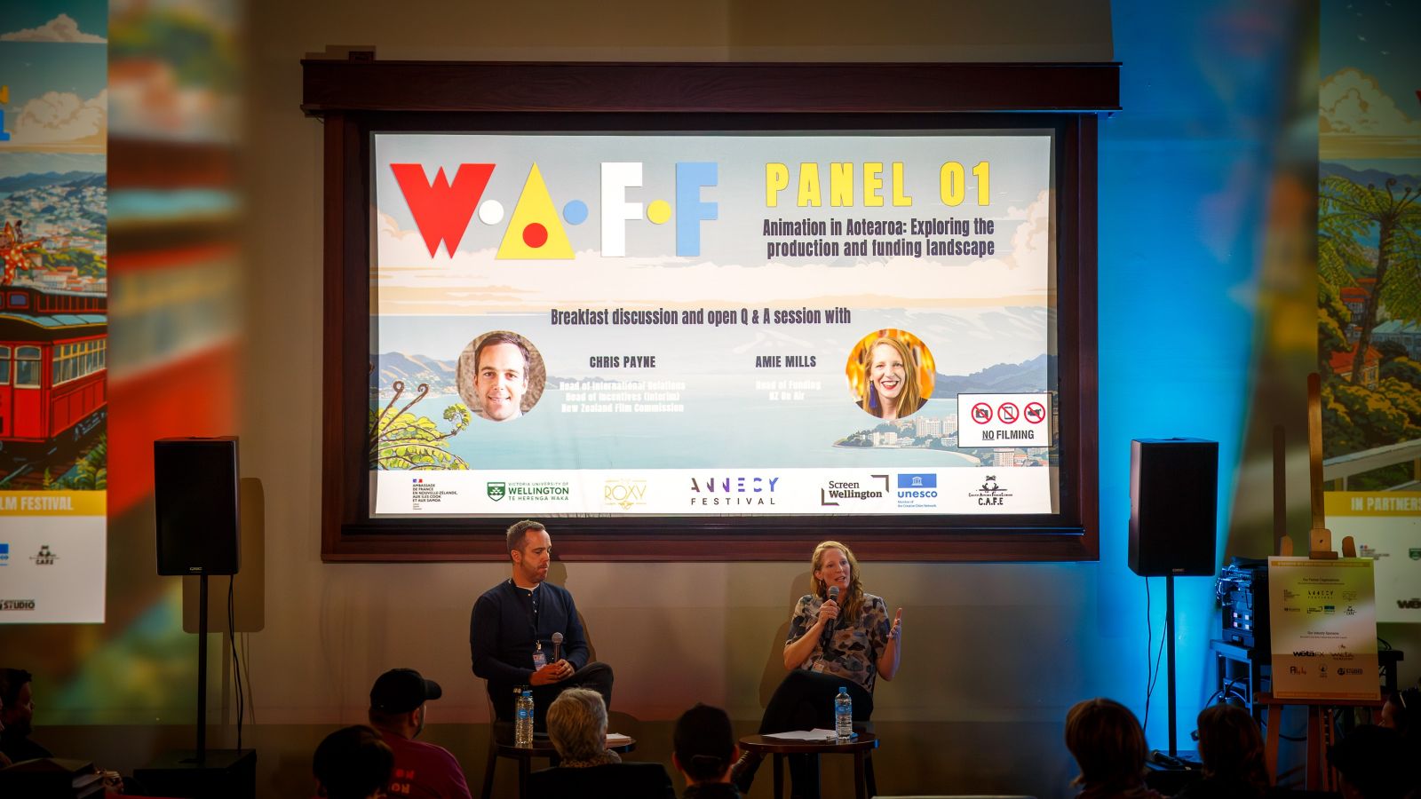 Two panelists, Chris Payne and Amie Mills on stage at Roxy Cinema, engaging with a small audience. 