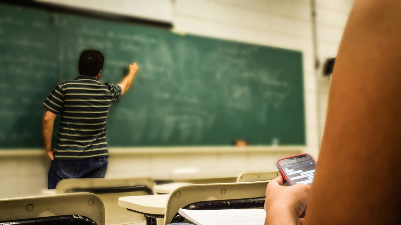 Teacher in classroom writing on a chalkboard