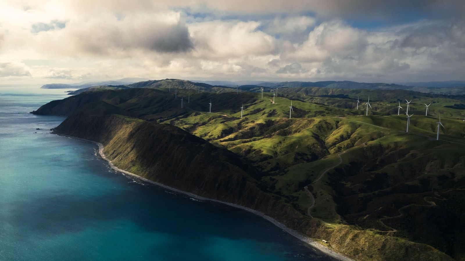 Beautiful blue ocean with green-covered land beside it, covered in wind turbines
