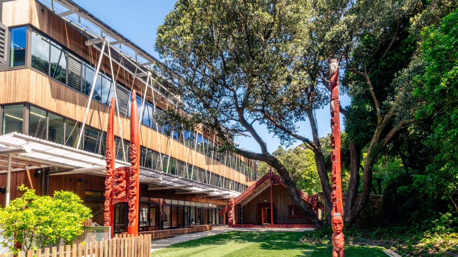 Nga mokopuna Building with wooden exterior on left of shot, with māori carvings visible and a marae in the middle distance