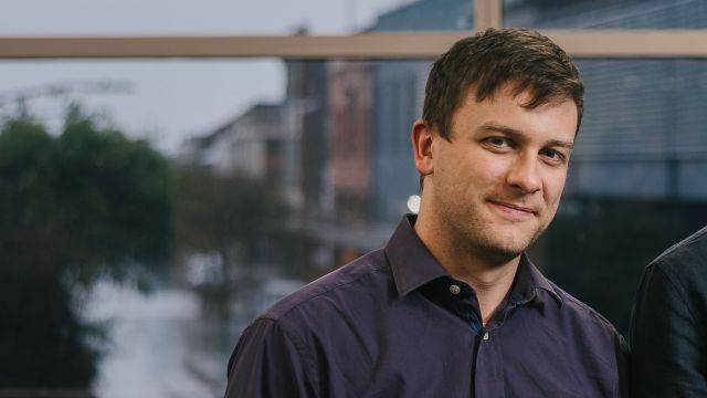 Man wearing dark blue top smiling slightly at camera