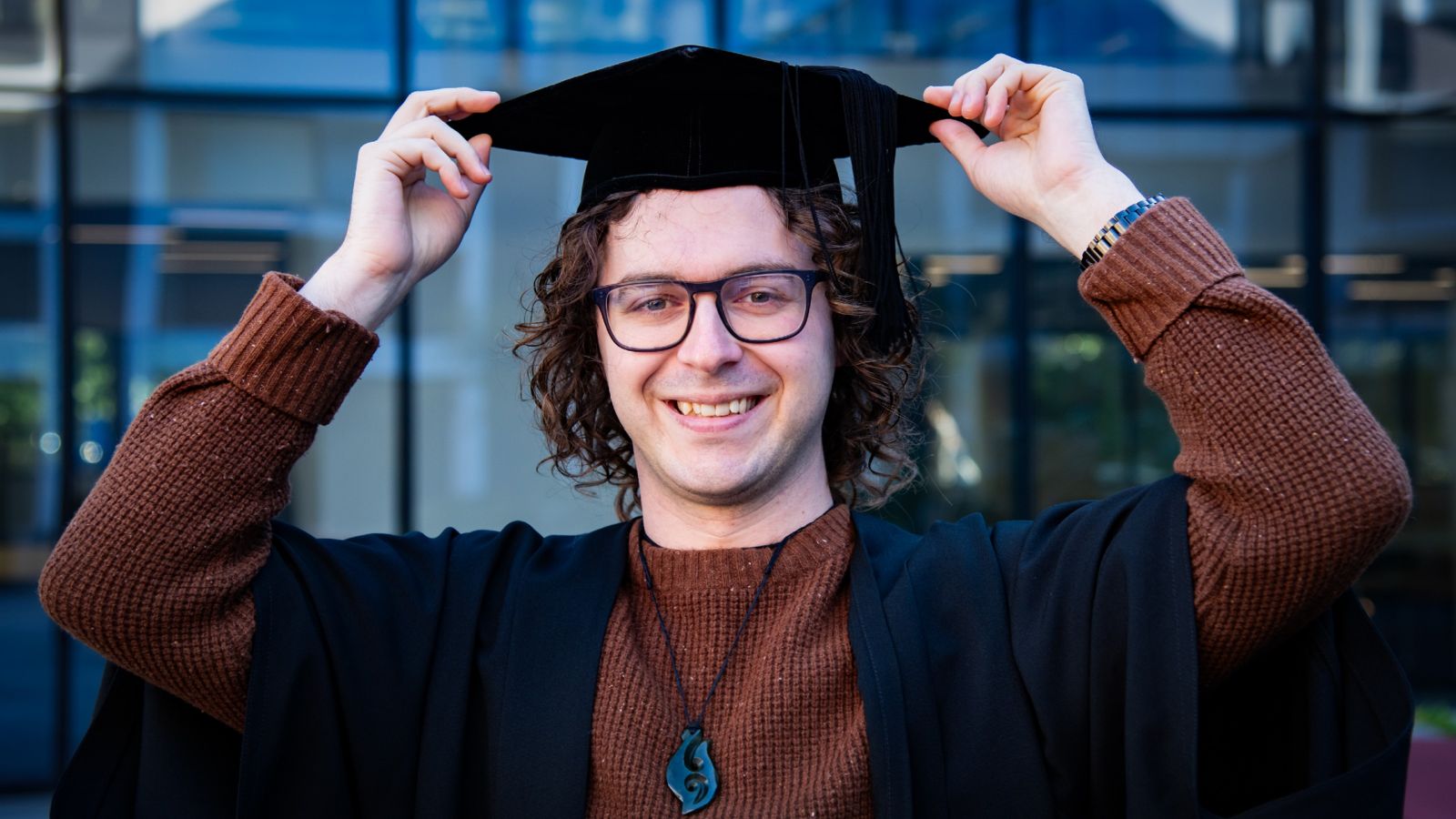 Wearing his graduation robes, Philip poses for a photo in the Cotton Plaza on Kelburn campus. 