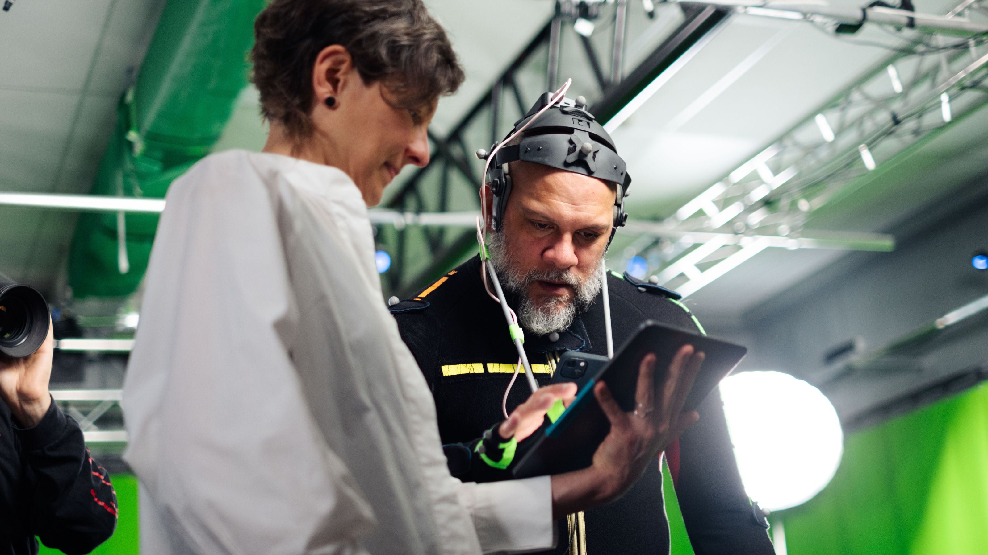 Woman in white shirt showing an ipad screen to a man in a motion capture suit