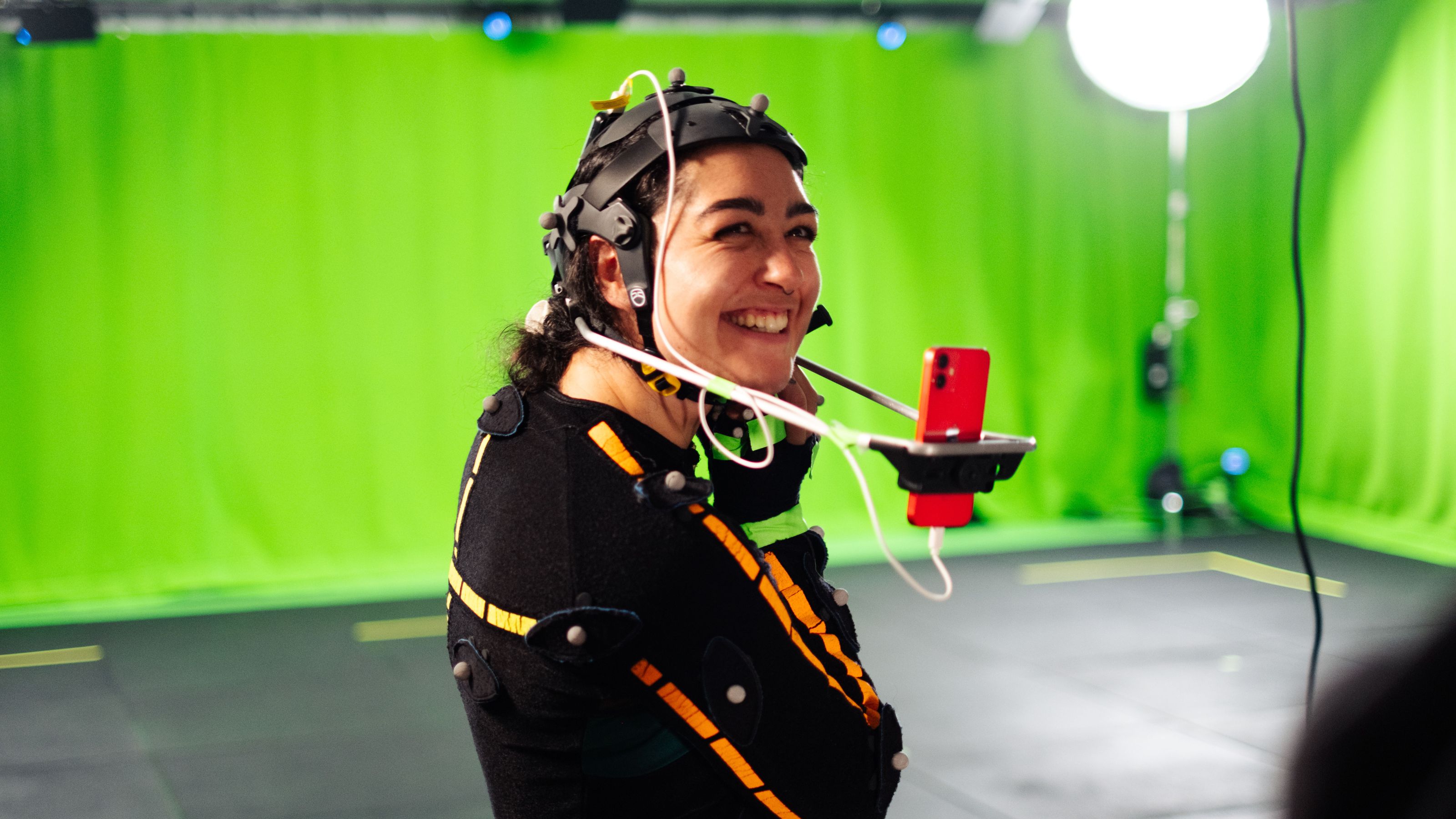 Girl wearing motion capture suit smiling widely, smartphone in front