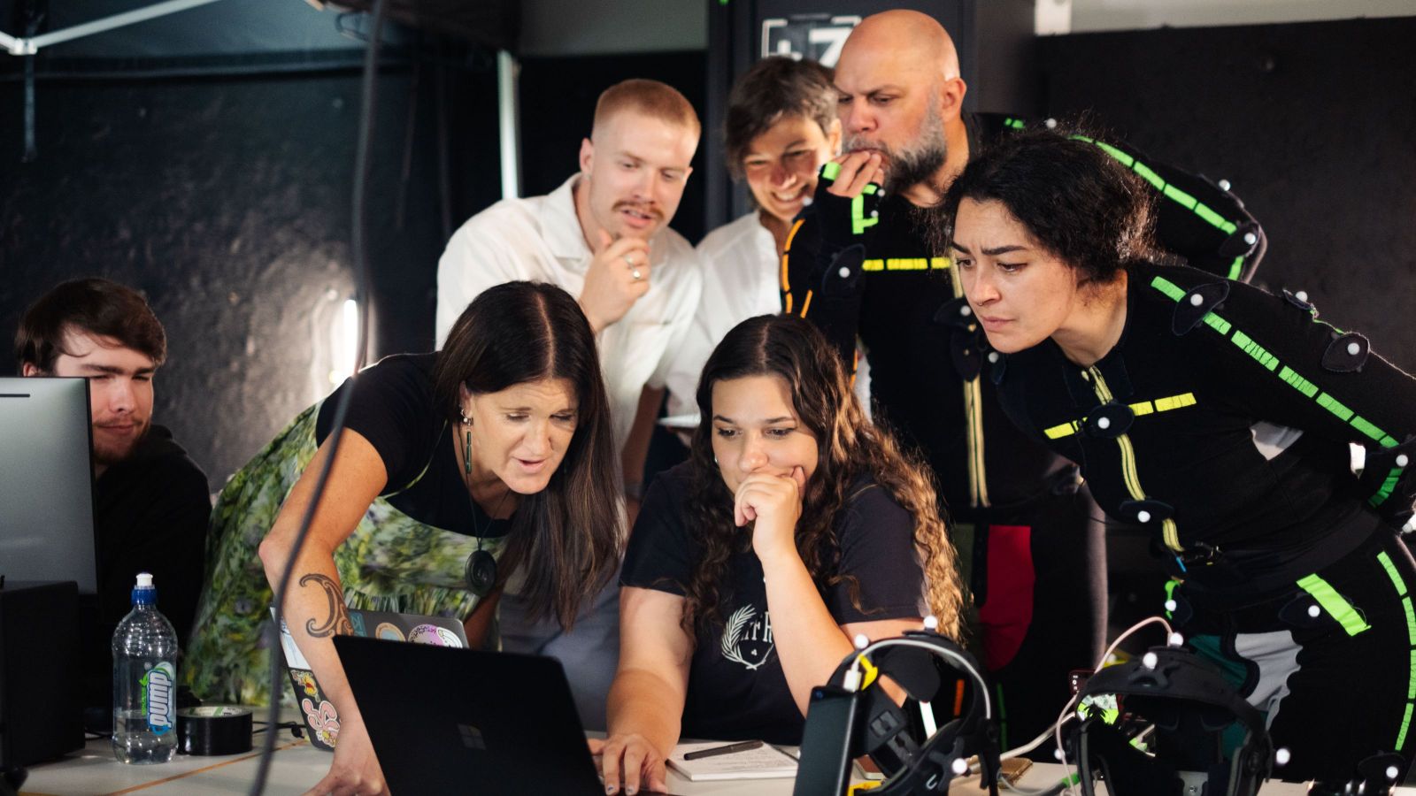 group of 8 people, two wearing motion capture technology suits, around a computer