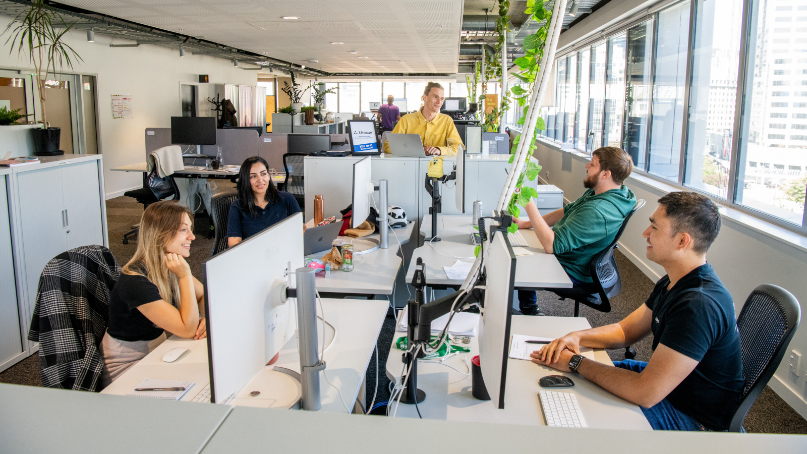 Five people are sitting at computers in a brightly lit room.