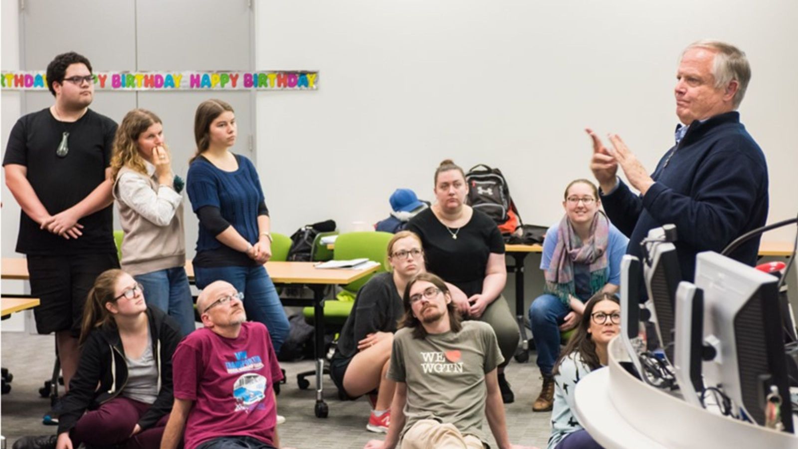 Man with grey hair teaching sign language at front of a class of students