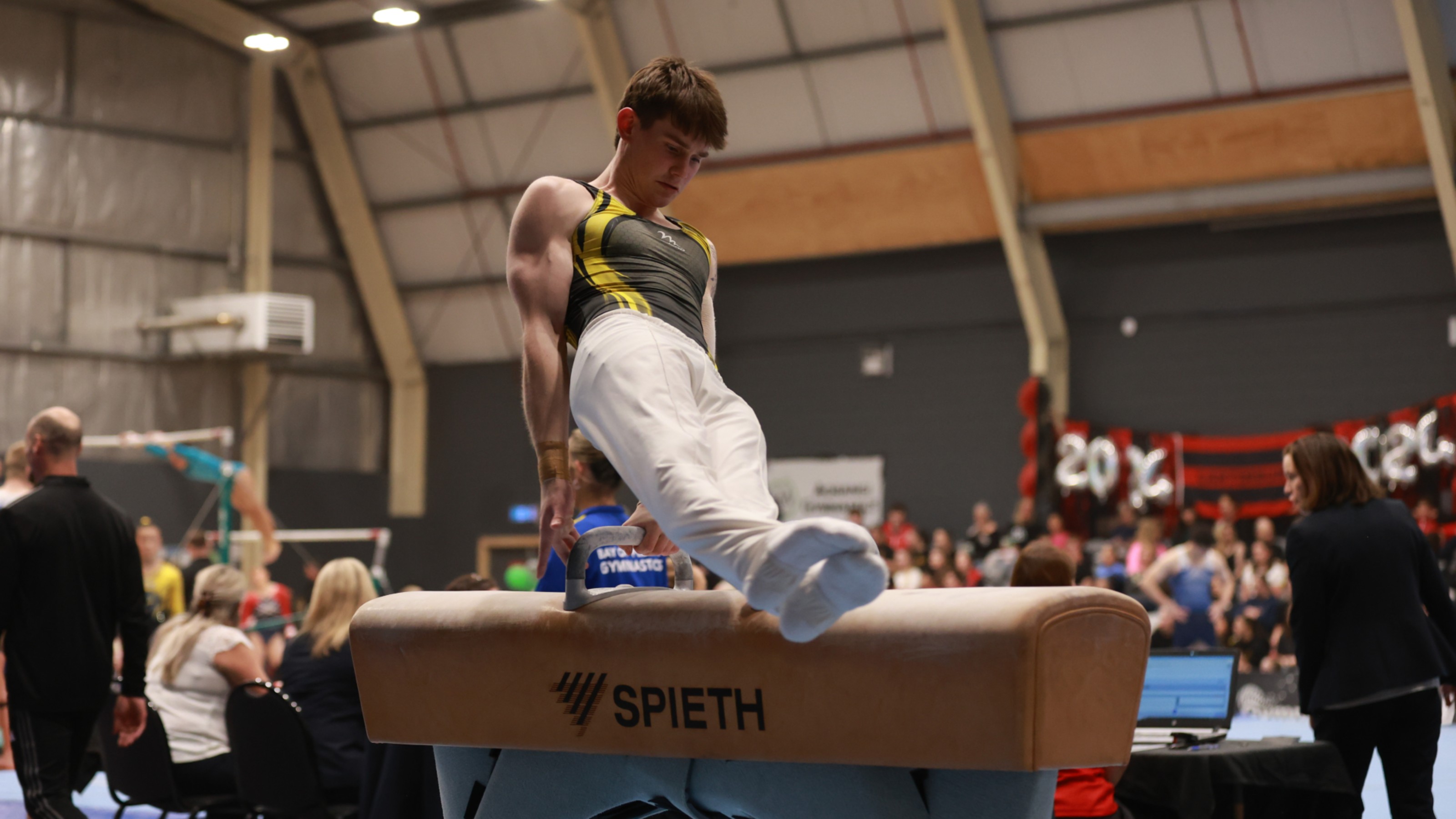 Young man swinging across a pommel horse inside a gymnasium