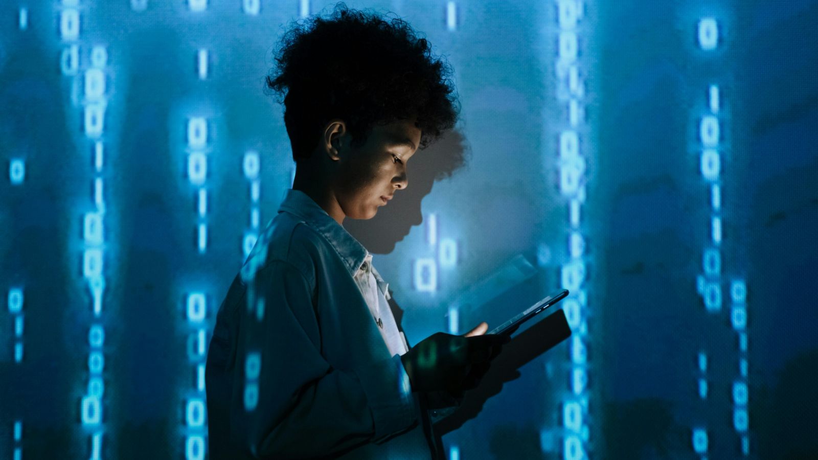 Young person holding a tablet and standing against a projection of numbers