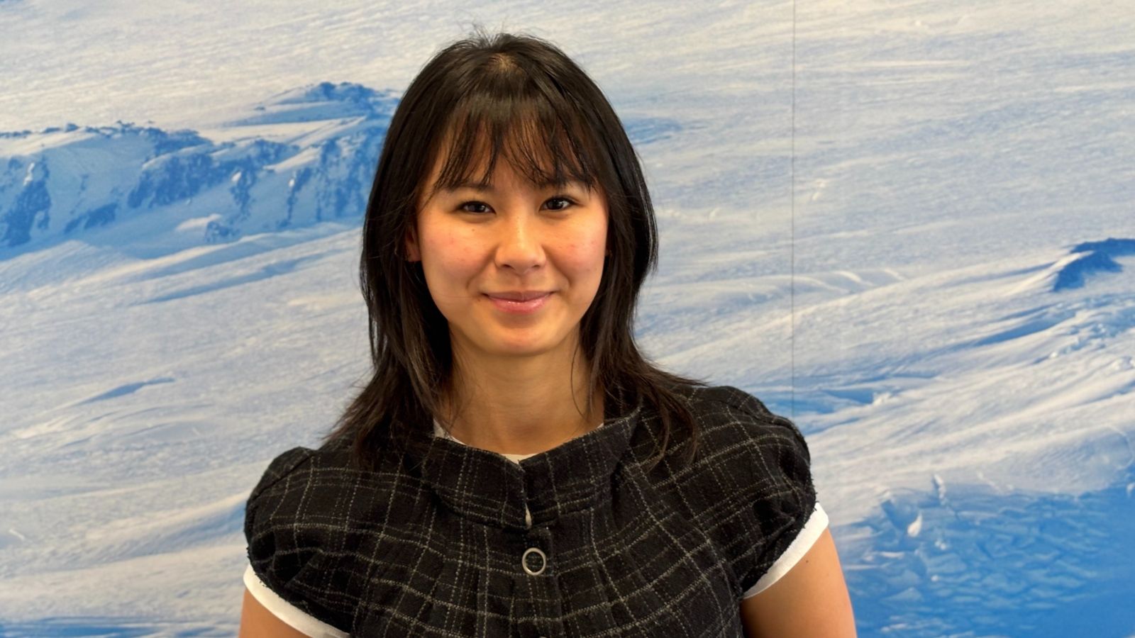 Young woman smiles in front of large picture of ice landscape.