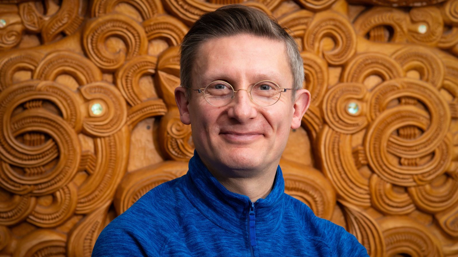 Man in blue merino top against ornate wooden carved background