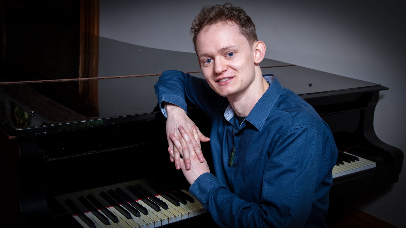 Ethan Hotter sitting at a piano smiling at the camera.