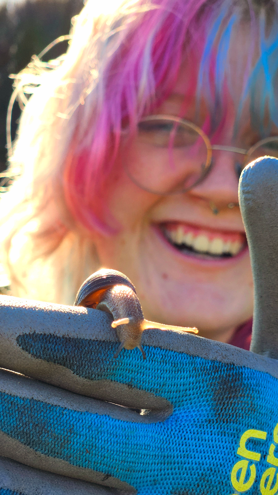 Person with pink hair smiling holding a snail