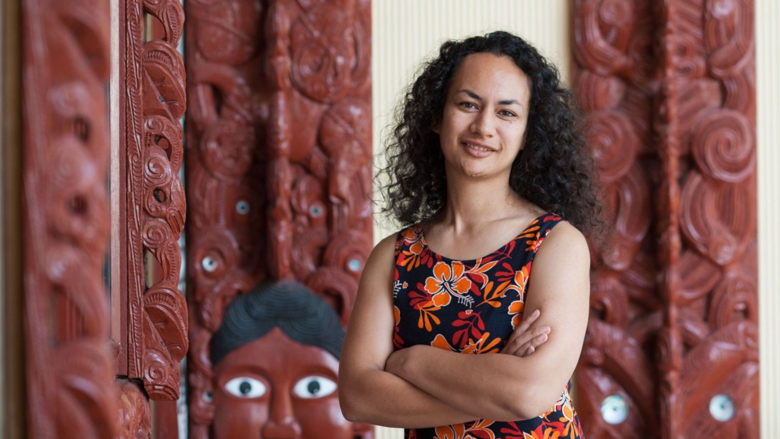 Woman with dark curly hair standing in front of a marae