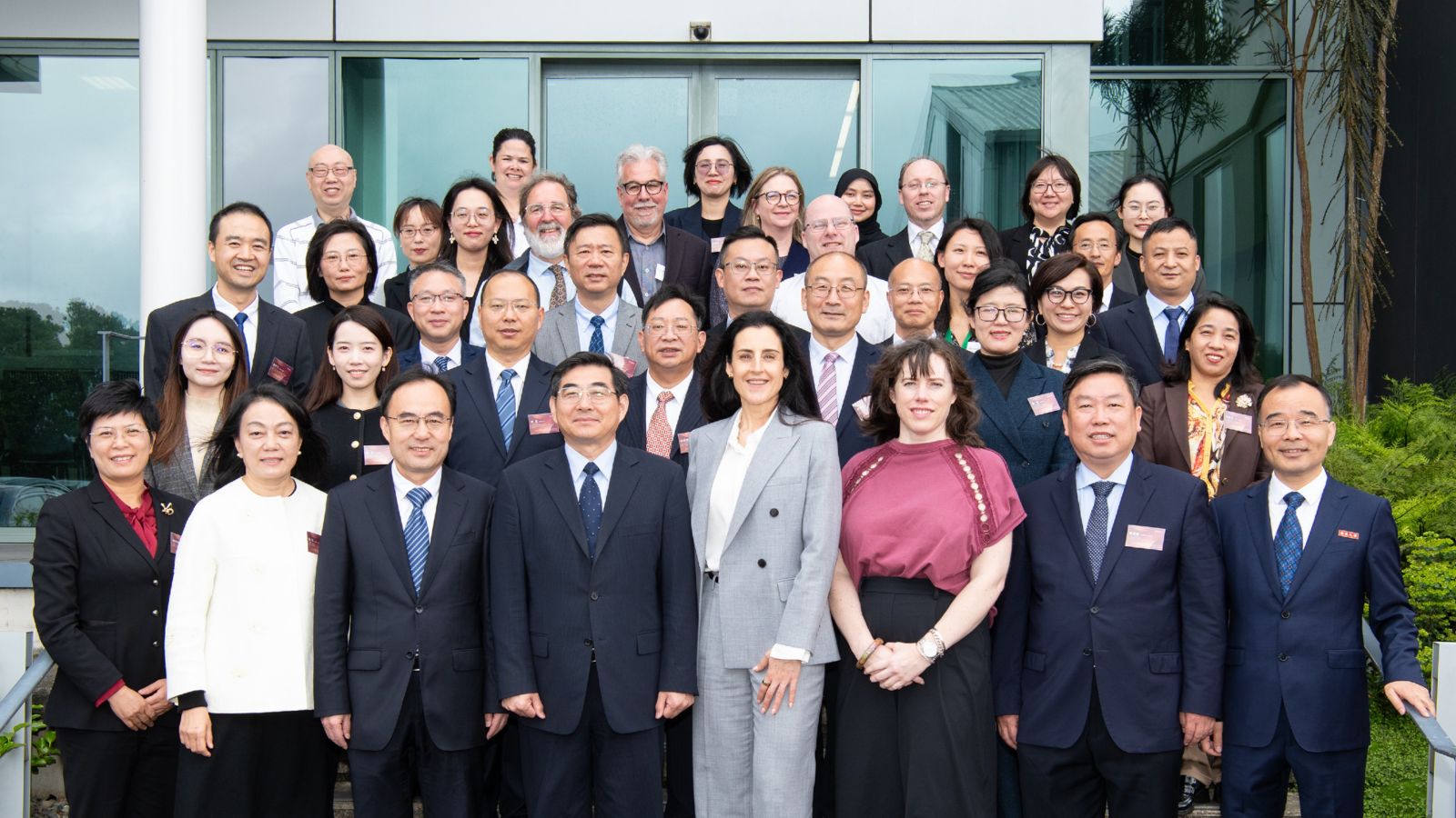 A large group of people stand outside a building on steps and smile at the camera.