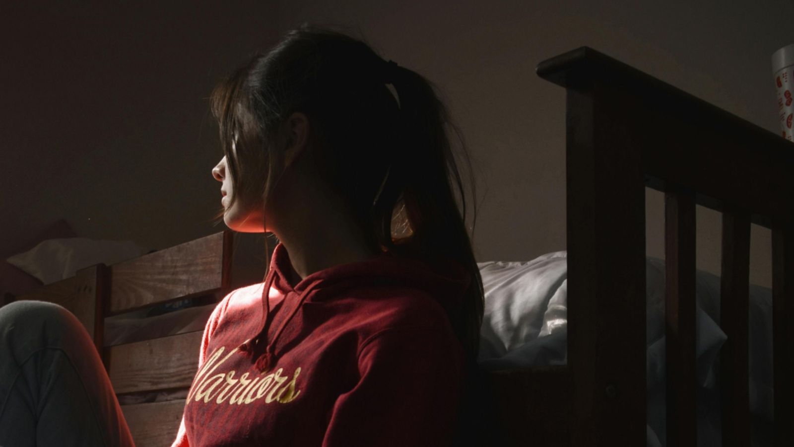 Young woman in bedroom, sitting on floor and looking out the window