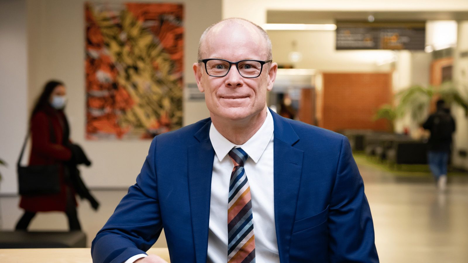 person in blue suit, wearing tie, looking straight at the camera
