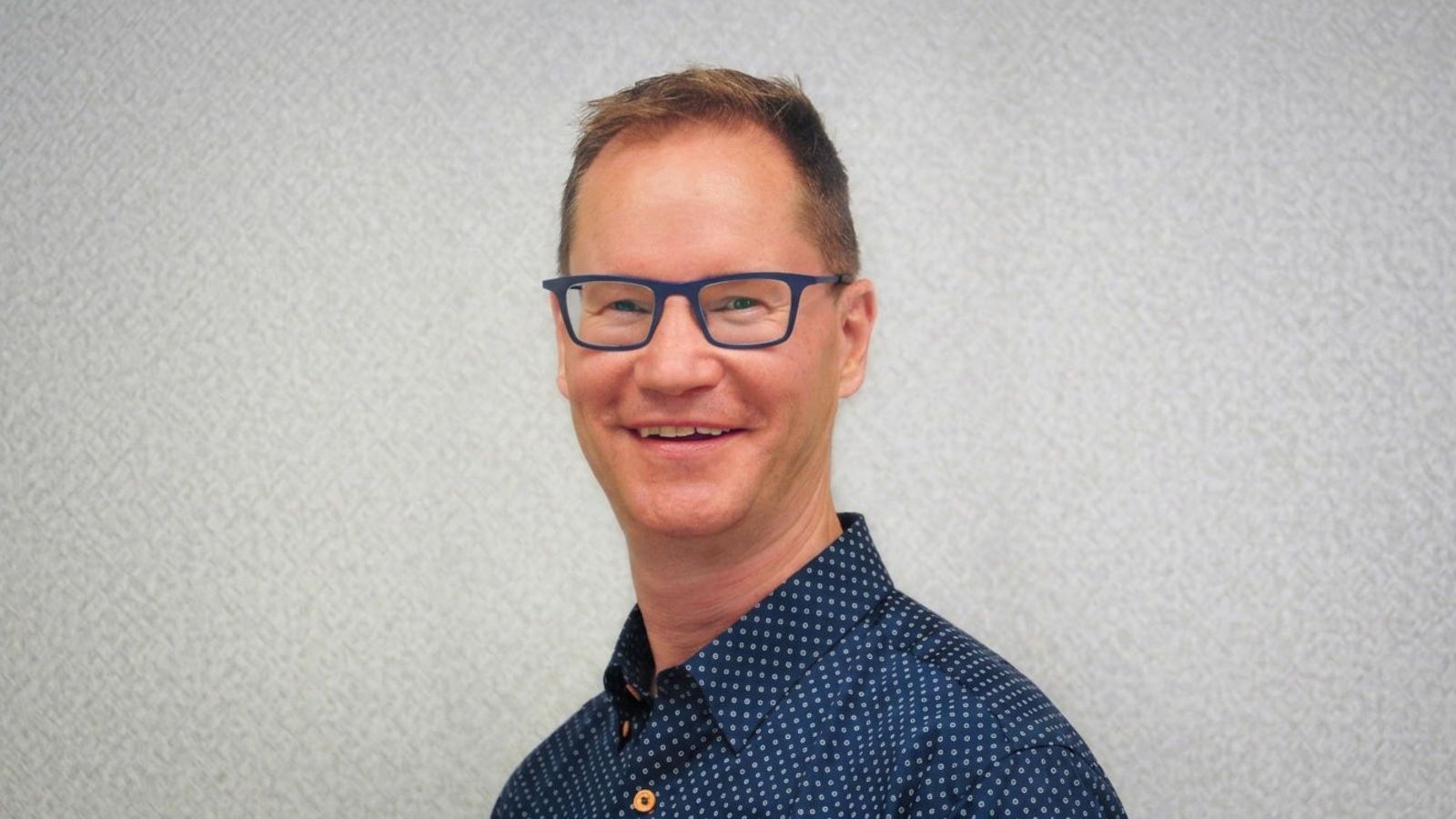 Headshot of a man in glasses smiling at camera