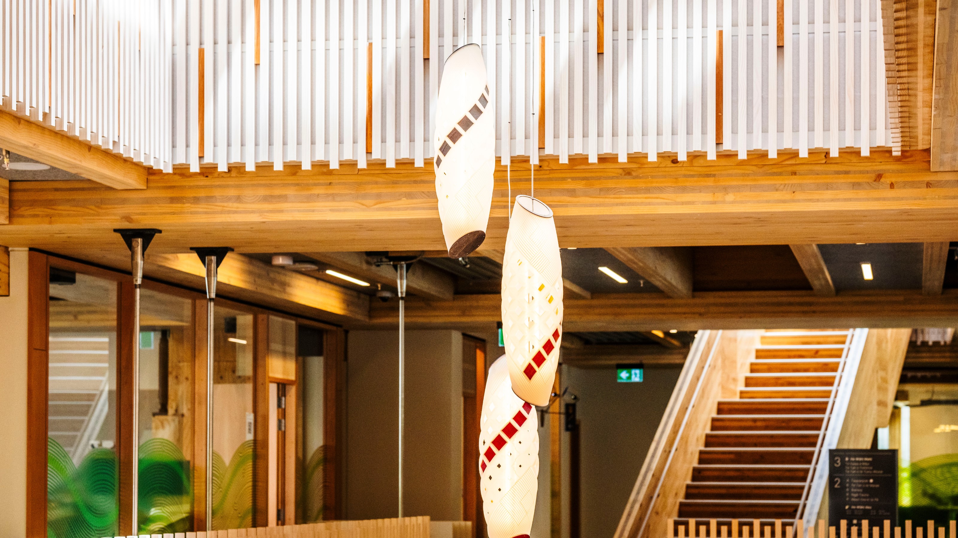 Atrium of a modern building showing light coloured mass timber and hanging light feature