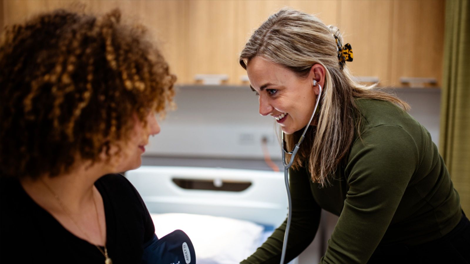 Smiling woman with a stethoscope, with a woman's profile in foreground