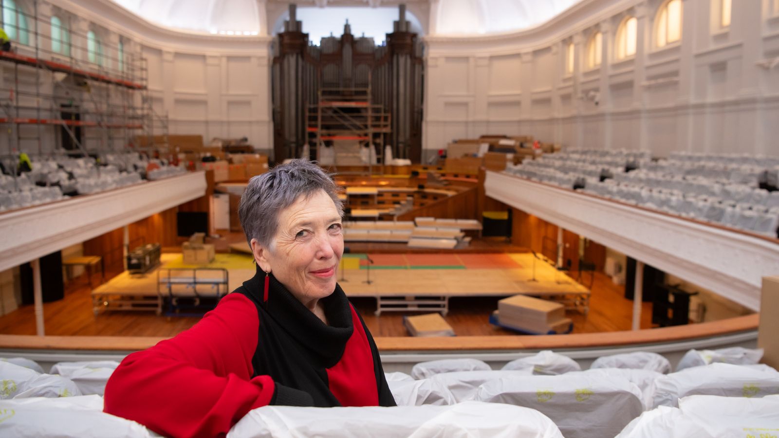 Sally Jane Norman sitting on a chair in the Adam Auditorium in the under-construction Town Hall.