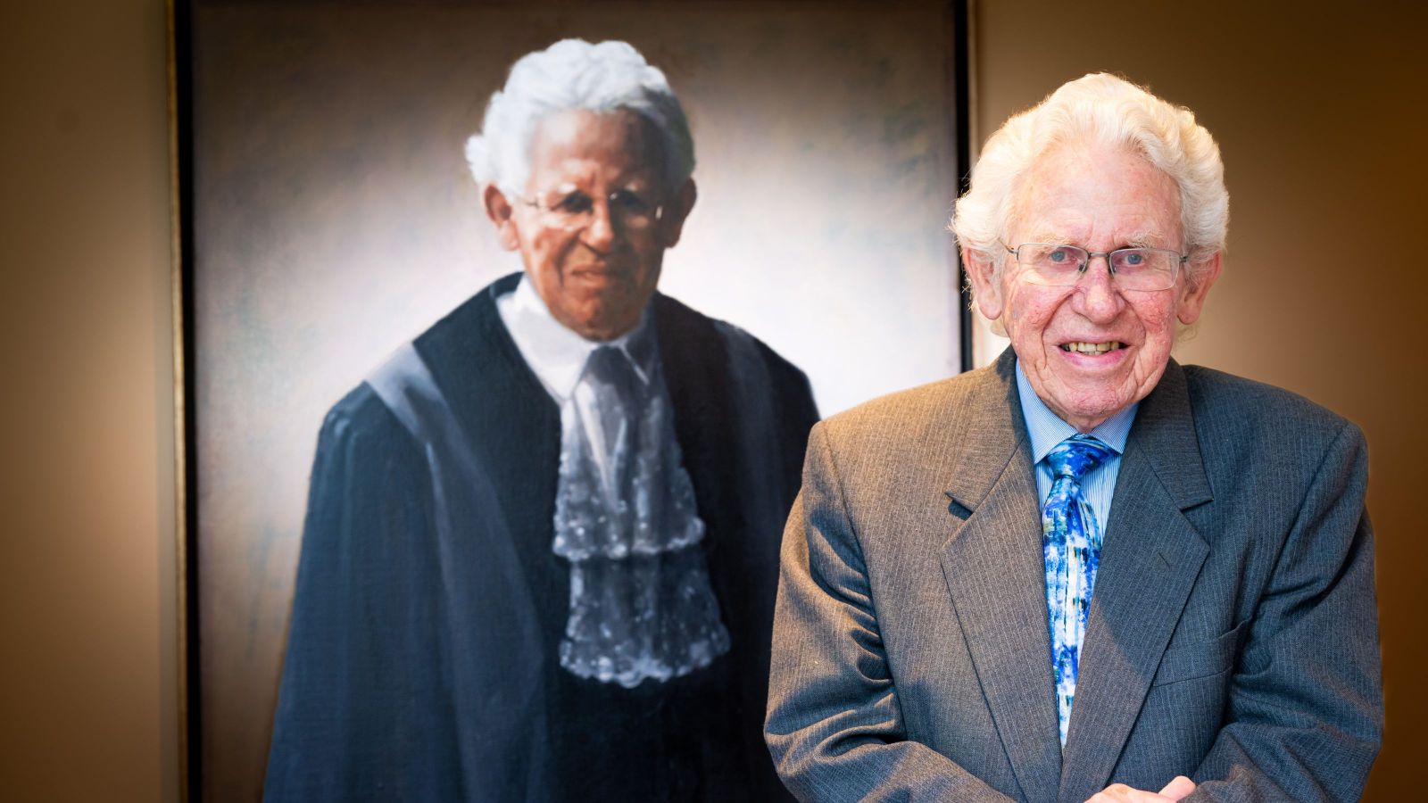 man with white curly hair standing in front of painted portrait of himself