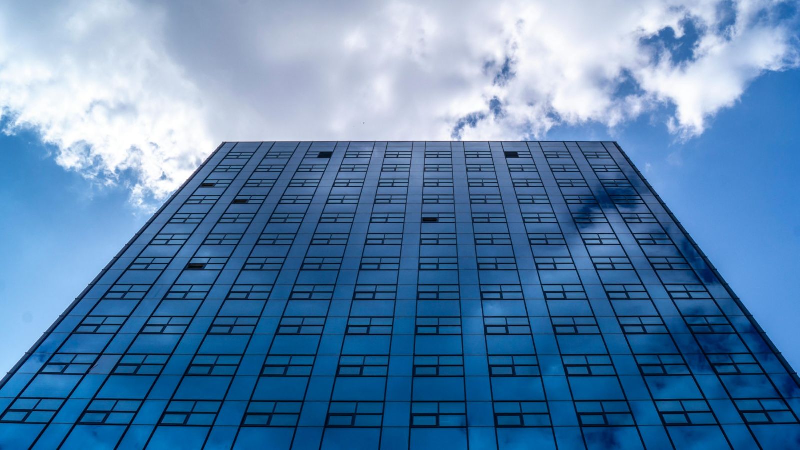 Glass-fronted office building with clouds in sky above 