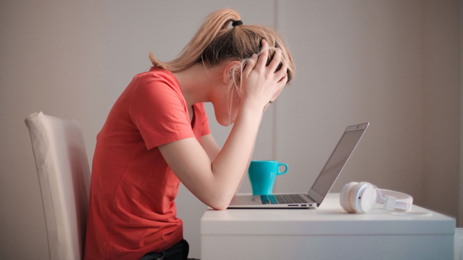 Young woman sitting at desk with head in hands, looking at a laptop