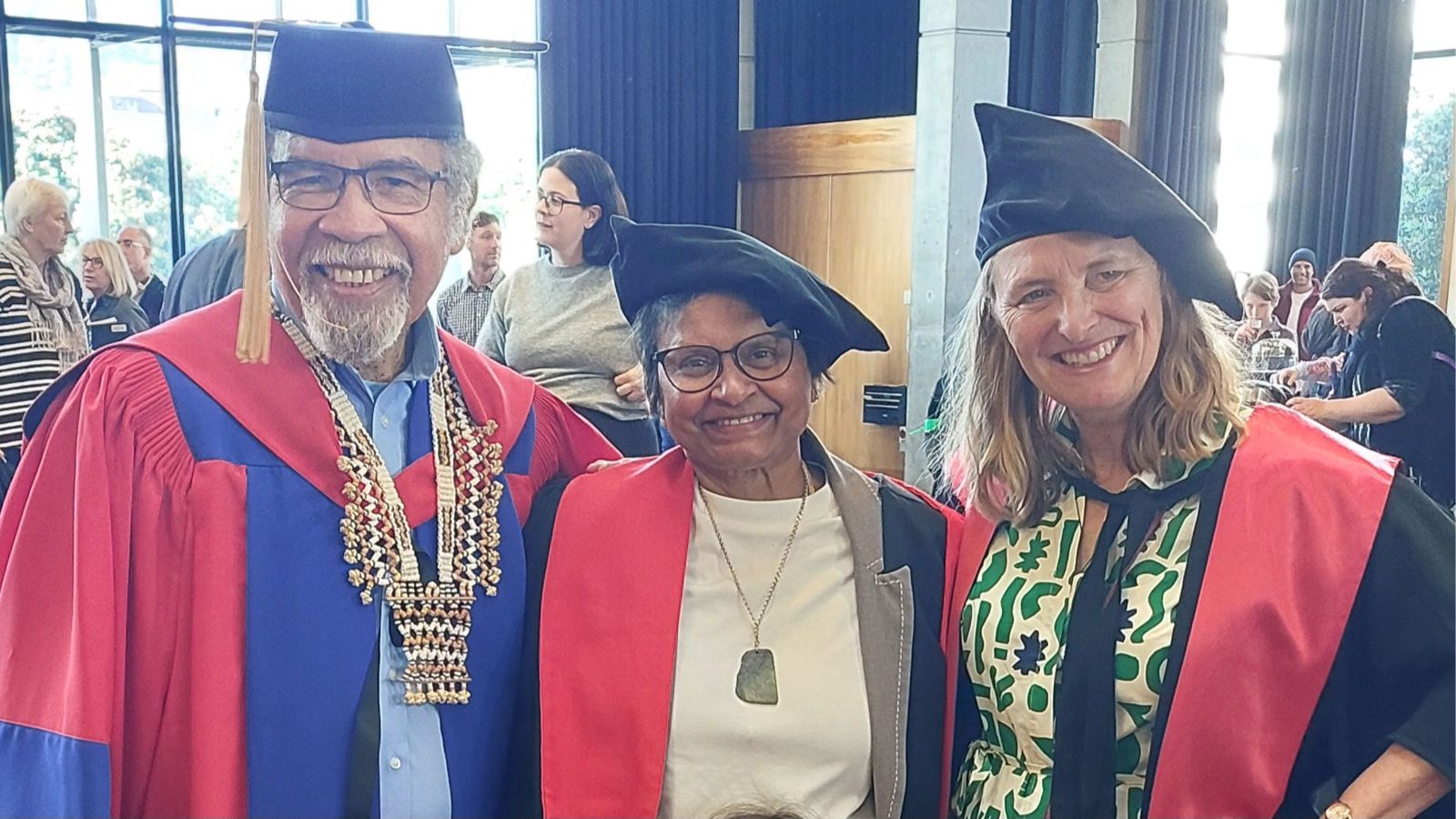 three people in full academic dress, one with a blue and red doctoral robe, two others with doctoral robes