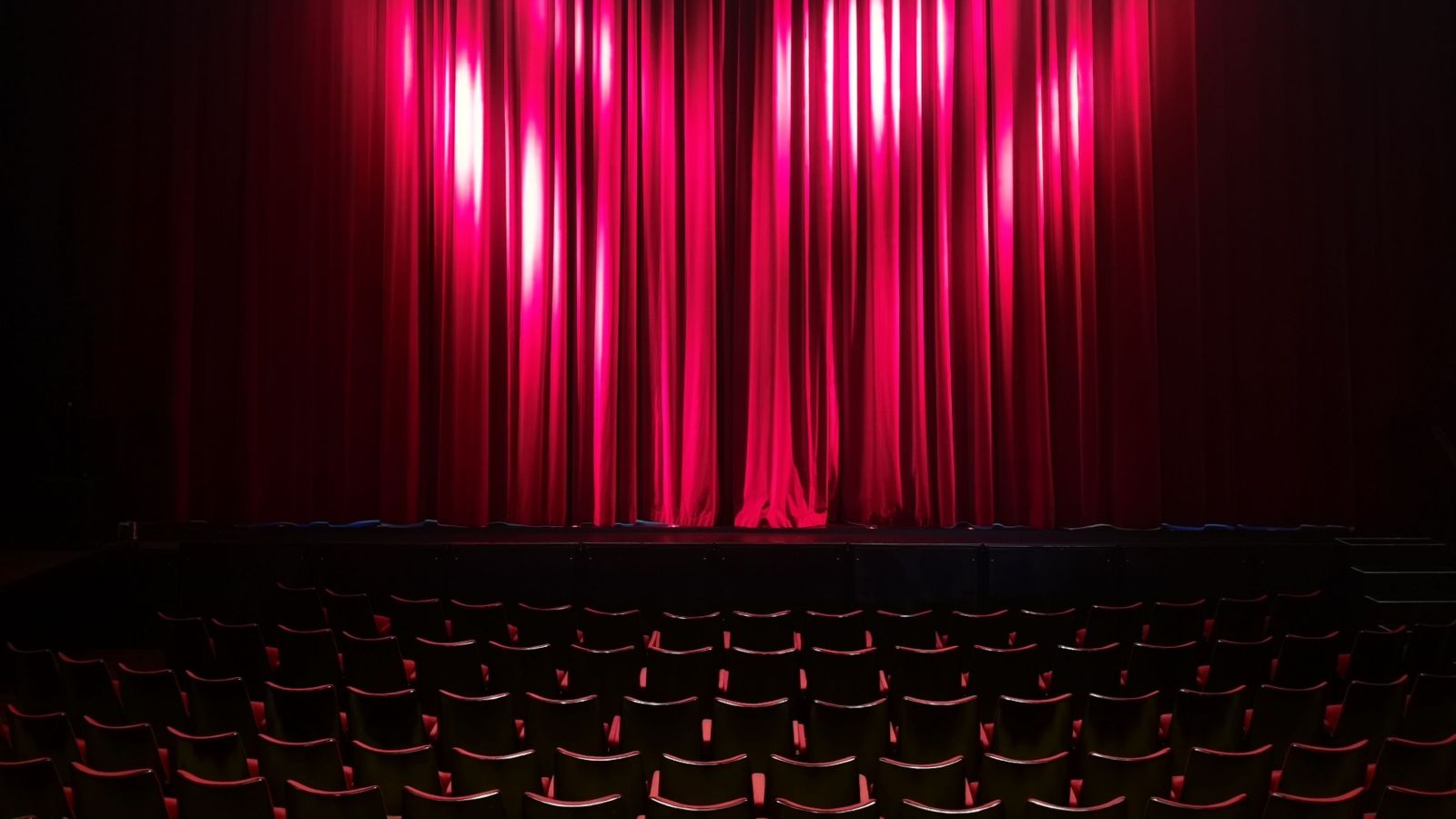 Theatre stage with red curtain and empty seats in the foreground 