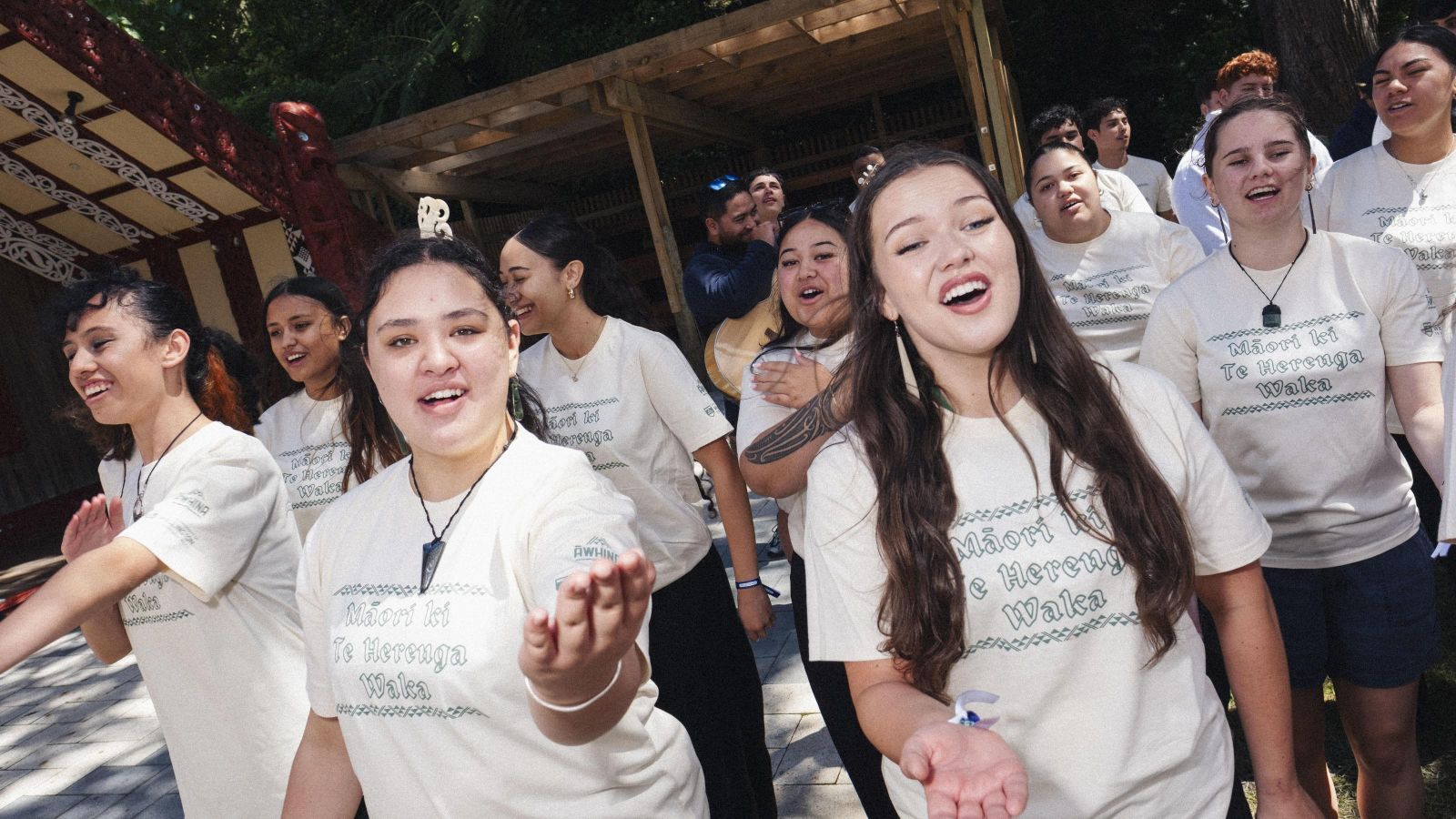 Large group of students wearing same tops in front of marae
