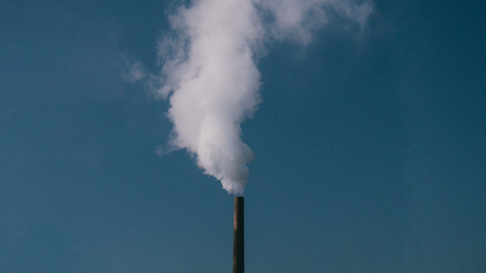 Industrial chimney emitting smoke against a blue sky