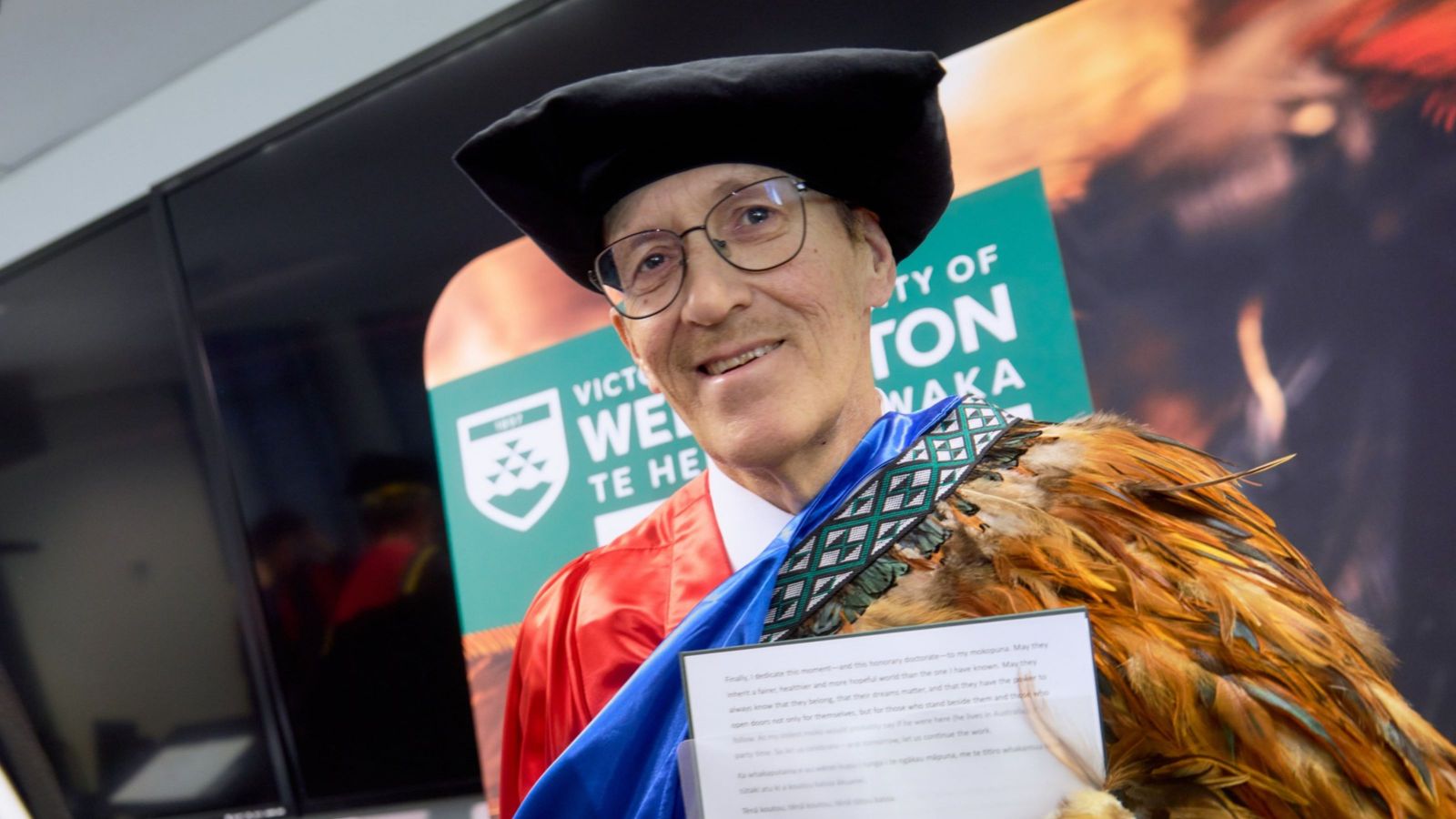 man wearing doctoral robes and bonnet alongside a maori feathered cloak