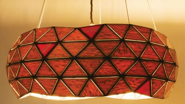 Image of an interior light with a geomtric shade made of triangles. The light hangs from a ceiling and is giving off a warm light.